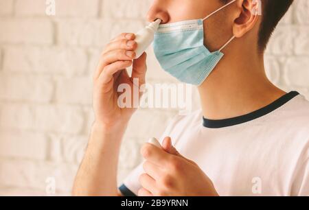 Closeup di giovane con malattia usando spray nasale per il suo naso congestionato. Sicuro medico malato in maschera medica protettiva sul viso utilizzando gocce nasali Foto Stock