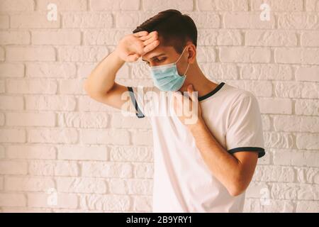 Ritratto di giovane malato in maschera medica protettiva che soffre di alta temperatura corporea. Uomo malato che ha mal di testa e febbre come sintomi di c Foto Stock
