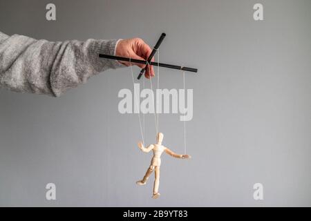 La mano umana tiene una bambola di legno sulla linea di abbigliamento su uno sfondo grigio con posto per il testo. Concetto di metafora di potenza Foto Stock