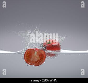 i pomodori cadono nell'acqua spruzzando intorno. concetto di alimento fresco e naturale. rendering 3d. nessuno intorno Foto Stock