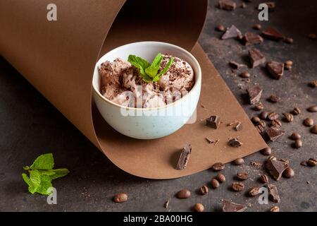 Gelato al cioccolato con patatine di cioccolato, chicchi di caffè e menta fresca in carta swirl su sfondo marrone Foto Stock