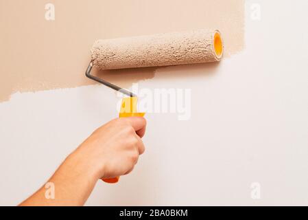 Riparazione in casa. Un uomo dipinge le pareti con un rullo di colore beige Foto Stock
