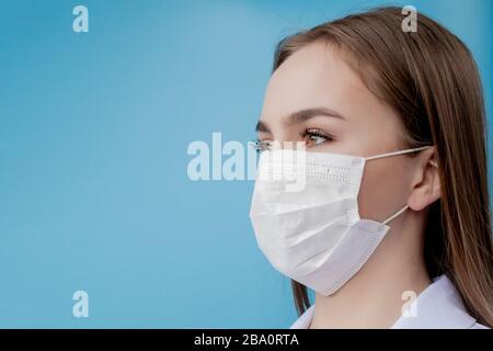 Infermiere medico sorridente dietro maschera chirurgo. Primo piano ritratto di giovane donna caucasica modello su sfondo blu. Donna che indossa la massa per proteggere covid-19 Foto Stock