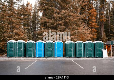 Fila di bagni chimici portatili verdi e blu nella foresta autunnale al parco nazionale Foto Stock