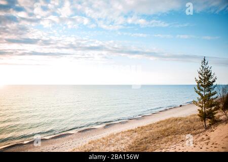 Sedendosi su una spiaggia sola per guardare il tramonto sull'acqua distanza sociale Foto Stock