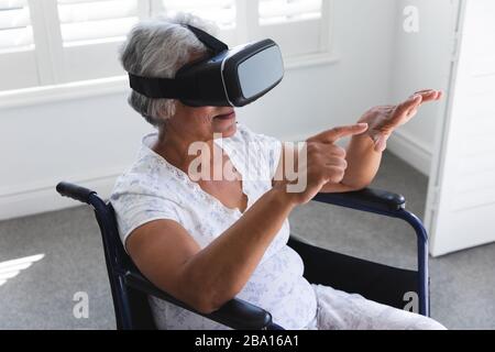 Vista laterale di una donna afroamericana seduta su una sedia a rotelle e utilizzando la realtà virtuale Foto Stock