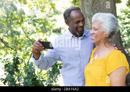 Vista laterale di una coppia afroamericana che prende un selfie in giardino Foto Stock