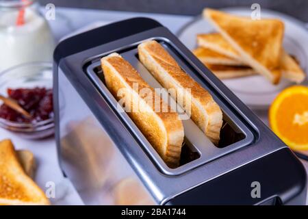 Fette di ottimo pane tostato uscenti dal tostapane. Cucina sana per la colazione e tecnologia di riscaldamento. Mettere a fuoco su fetta di grande. Foto Stock