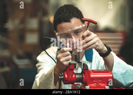 un riparatore in un negozio di riparazione auto regola un dado in una morsa. regolazione tonale colore Foto Stock