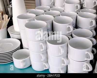 Esposti su pile di tazze bianche e piattini in ceramica pulita. I piatti del ristorante sono preparati per bere il tè e il caffè. Foto Stock