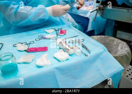 Strumenti chirurgici sterili e contenitori in vetro con soluzioni sul tavolo durante un intervento chirurgico. Sopra la tabella sono le mani di un chirurgo Foto Stock