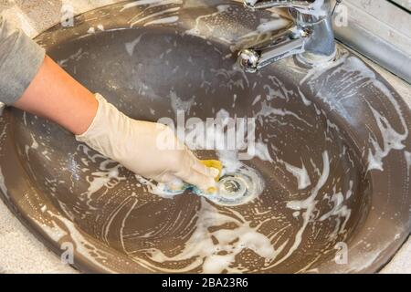 Pulizia profonda efficace del bagno con disinfettante per ridurre il rischio di infezioni comuni. Femmina con guanti sfrega con lavello in spugna con detergente. Foto Stock