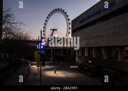 Londra, Regno Unito. 25 Marzo 2020. Una figura solitaria illuminata da luci di strada attraversa al crepuscolo una Royal Festival Hall vuota, mentre il ‘Coronavirus Lockdown' del West End di Londra continua ad affrontare la rapida diffusione della malattia in tutta la capitale. Gli economisti prevedono anche un crollo economico dovuto alle restrizioni e la chiusura di teatri, ristoranti e negozi potrebbe costare più vita di Cronavirus. Credit: Jeff Gilbert/Alamy Live News Foto Stock