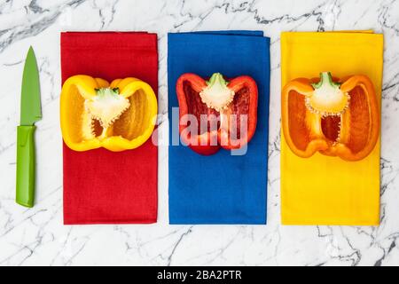 peperoni gialli, arancioni e rossi con coltello da parare su bancone in marmo Foto Stock