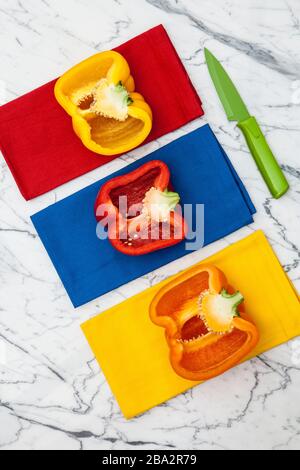 peperoni gialli, arancioni e rossi con coltello da parare su bancone in marmo Foto Stock