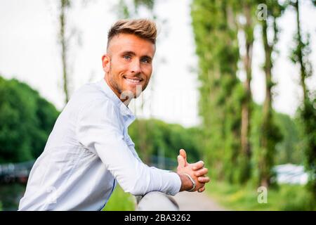 Felice biondo giovane uomo appoggiato sulla recinzione Foto Stock