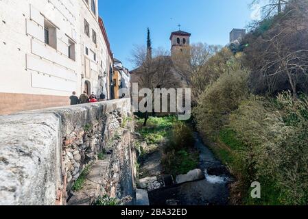 Il fiume Darro sulla sua strada attraverso Granada con un ponte e la gente a piedi su Carrera del Darro Street Foto Stock