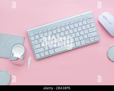 Concetto di blog di bellezza. Uno spazio di lavoro donna, tastiera di un computer e mouse vicino a un contenitore viso crema isolato su uno sfondo rosa con spazio copia. Foto Stock