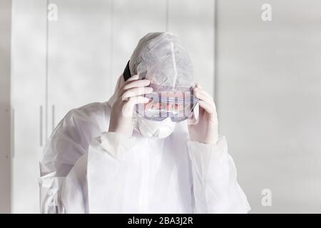 Medico stanco con indumenti protettivi a causa di coronavirus in un ospedale - sfondo bianco brillante Foto Stock