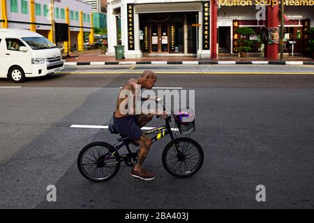 Il vecchio uomo cinese con i tatuaggi guida una bicicletta a Singapore Foto Stock