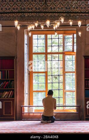 Uomo credente che prega davanti ad una grande finestra in una moschea, formato ritratto, Istanbul, Turchia Foto Stock