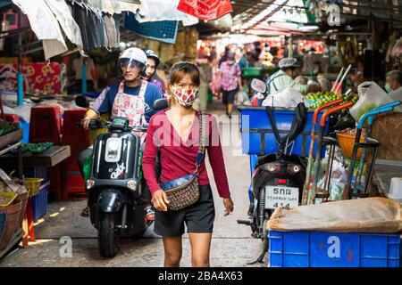 Bangkok, Thailandia - 03/17/20: Una giovane donna tailandese cammina attraverso Khlong Toei tradizionale Wet Food Market che indossa una maschera facciale protettiva. Foto Stock