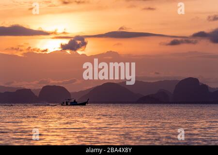 La sagoma di un peschereccio tailandese a coda di pesce che naviga tra lontane montagne durante un tramonto dorato vicino a Krabi, THAILANDIA. Foto Stock