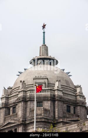 Shanghai, Cina - 4 maggio 2010: Primo piano della parte superiore grigio-marrone con cupola della banca HSBC con bandiera cinese rossa davanti, stella sulla parte superiore, contro il cielo d'argento. Foto Stock