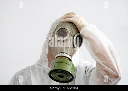 Uomo in indumenti protettivi e maschera di gas su sfondo bianco. Un lavoratore stanco in tuta protettiva. Affaticamento, dolore alla testa Foto Stock