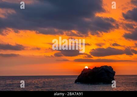 Tramonto su una roccia solitaria in un mare calmo. Colori incredibili nel cielo nuvoloso Foto Stock