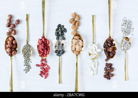 Cucchiai dorati con varie superfici su sfondo di legno bianco vista dall'alto. Concetto di alimentazione sana. Foto Stock