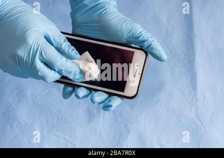 Sanitizzando un telefono cellulare, una donna applica uno spray antisettico a base di alcol a un rubinetto per prevenire la diffusione del virus Foto Stock