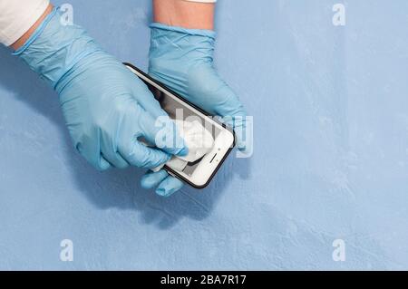 Sanitizzando un telefono cellulare, una donna applica uno spray antisettico a base di alcol a un rubinetto per prevenire la diffusione del virus Foto Stock