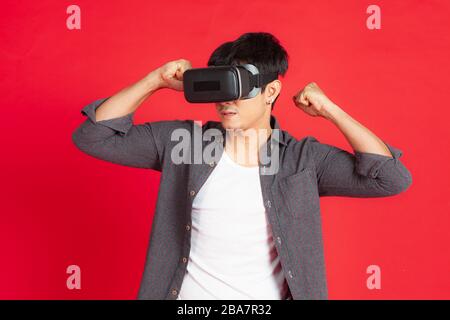 Giovane uomo Che Indossa visore VR ed esplora un altro mondo isolato su sfondo rosso Foto Stock