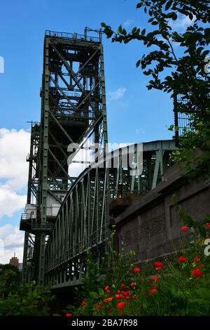 Rotterdam, Paesi Bassi - Luglio 2019; vista a bassa angolazione dell'iconico ex ponte ferroviario ‘de hef’ con papaveri in prima linea e cielo blu Foto Stock