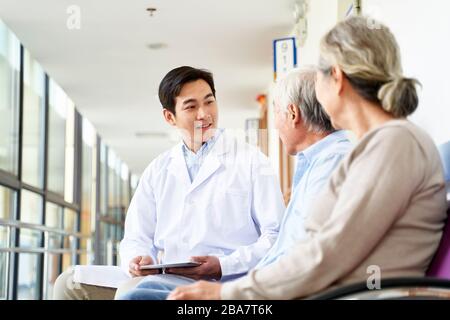 un giovane medico asiatico cordiale che parla con la vecchia coppia nel corridoio dell'ospedale Foto Stock