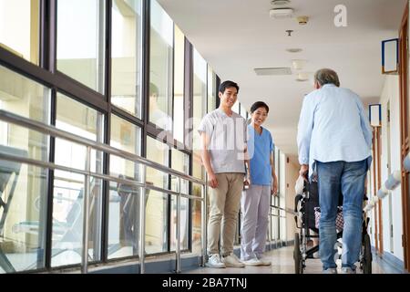 giovani terapisti asiatici felici che salutano i residenti nel corridoio della casa di cura Foto Stock