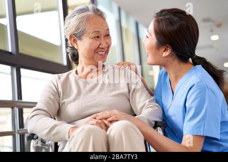 gentile operatore di casa di cura che parla con la donna asiatica senior in corridoio Foto Stock