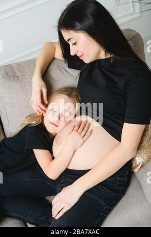 Mamma dolce incinta con figlia sul divano. Giovane bella donna incinta con la sua bambina carina. Vista dall'alto. Foto Stock