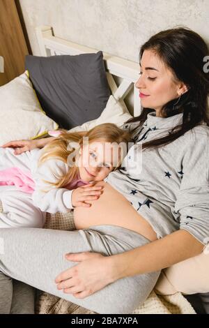 Bambina messo mano su mamma incinta tummy, famiglia felice di due e secondo concetto di gravidanza Foto Stock