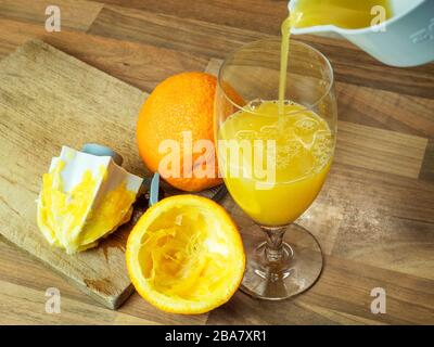 Versando il succo d'arancia appena spremuto in un bicchiere con un'arancia intera e mezza spremuta d'arancia su un piano di lavoro della cucina Foto Stock