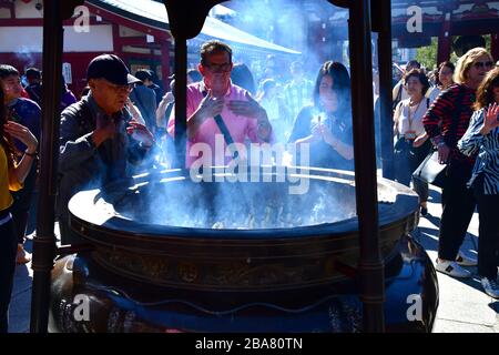 Persone intorno al bruciatore di incenso al tempio di Sensoji ad Asakusa, Tokyo. Credere è il fumo dal bruciatore di incenso ha un effetto healing. Foto Stock