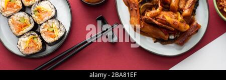 scatto panoramico di tteokbokki fresco e gimbap coreano su bianco e cremisi Foto Stock