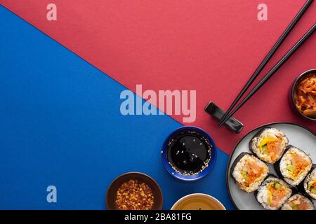 vista dall'alto della salsa di soia e dell'olio di sesamo vicino al gimbap su cremisi e blu Foto Stock