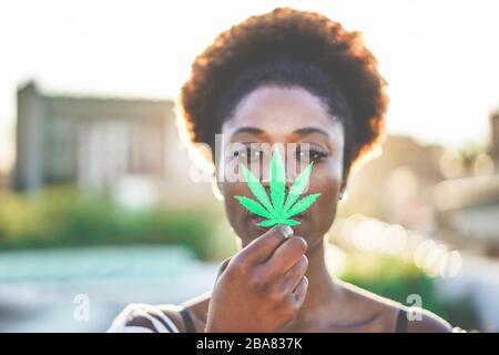 Giovane ragazza africana che tiene la foglia di marijuana con - Cannabis medicina, stile di vita sano e concetto di ecologia - Focus on leaf Foto Stock