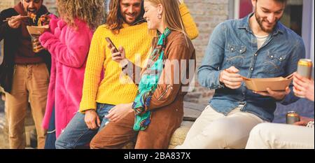 Amici felici mangiare cibo di strada all'aperto - giovani alla moda persone che si divertono insieme utilizzando telefoni cellulari e birre da bere - stile di vita della città e con festa Foto Stock