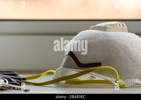 Maschera per respiratore N95 con chiavi e portafoglio su un bancone a casa. Dispositivi di protezione individuale.