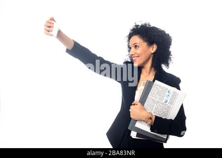 Donna d'affari afro-americana con documenti che prendono selfie e sorridendo isolato su bianco Foto Stock