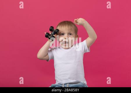 Un bambino tiene in mano una macchina da scrivere con le ruote in avanti, gli ondeggia le mani e gli stacca la lingua, guarda la macchina fotografica. Studio girato su un Foto Stock