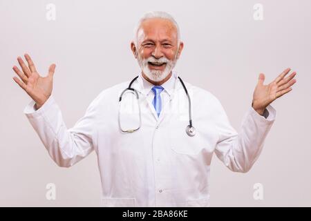 Medico senior felice e soddisfatto con braccia aperte su sfondo grigio. Foto Stock